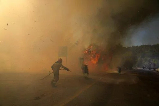 A firefighter tries to extinguish the flames next to motorcycles during a wildfire near Megara town, west of Athens, Greece, Wednesday, July 20, 2022. (AP Photo/Petros Giannakouris)
