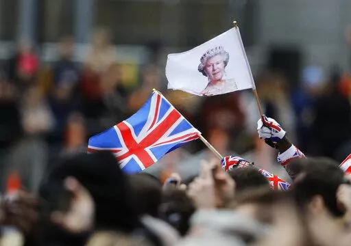 A man waves a British union flag and a flag bearing the image of Britain's Queen Elizabeth II ahead of the annual Commonwealth Day service at Westminster Abbey in London, Monday, March 9, 2020. After seven decades on the throne, Queen Elizabeth II is widely viewed in the U.K. as a rock in turbulent times. But in Britain’s former colonies, many see her as an anchor to an imperial past whose damage still lingers. (AP Photo/Frank Augstein, File)