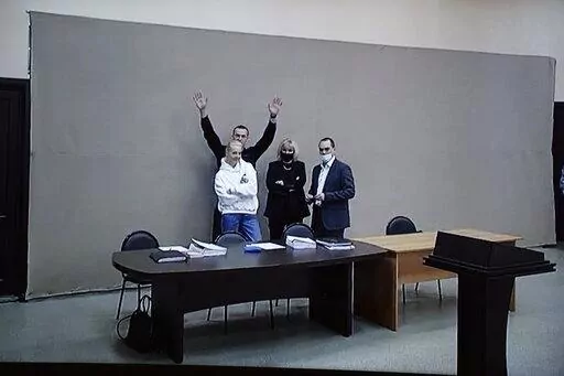In this image provided by the Russian Federal Penitentiary Service, Russian opposition leader Alexei Navalny waves to journalists and supporters via a video link, as he stands next to his wife Yulia and his layers during a court session in Pokrov, Vladimir region, about 100 kilometers (62 miles) east of Moscow, Russia, Monday, Jan. 17, 2022. A new trial against Russian opposition leader Alexei Navalny has opened at the penal colony where he already is serving a prison term. Navalny is charged wi