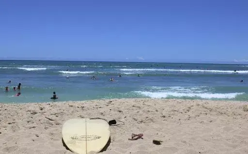 A surfboard lies on the sand on the sand at a beach known as White Plains in Ewa Beach, Hawaii, May 12, 2023. A judge has halted plans for an artificial wave pool until developers can revise an environmental assessment to address concerns raised by Native Hawaiians and others who say the project is unnecessary in the birthplace of surfing and a waste of water. (AP Photo/Jennifer Sinco Kelleher, File)