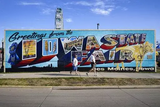 Fairgoers walk past a mural at the Iowa State Fair, Friday, Aug. 19, 2022, in Des Moines, Iowa. Potential White House hopefuls from both parties often swing by Iowa's legendary state fair during a midterm election year to connect with voters who could sway the nomination process. But this year, the traffic at the fair was noticeably light. Democrats are uncertain about President Joe Biden's political future and many Republicans avoid taking on former President Donald Trump. (AP Photo/Charlie Nei