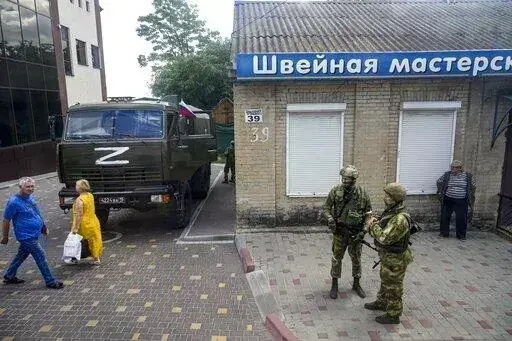 Russian soldiers guard an office for Russian citizenship applications as their military truck is parked nearby, in Melitopol, south Ukraine, on July 14, 2022. As Russians seized parts of eastern and southern Ukraine in the 8-month-old war, mayors, civilian administrators and others, including nuclear power plant workers, say they have been abducted, threatened or beaten to force their cooperation. In some instances, they have been killed. Human rights activists say these actions could constitute