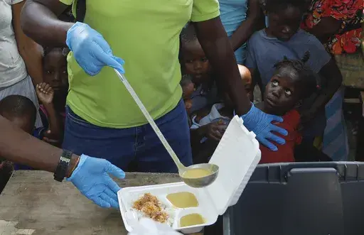 A server ladles soup into a container as children line up to receive food at a shelter for families displaced by gang violence, in Port-au-Prince, Haiti, March 14, 2024. Gang violence in Haiti has displaced over 300,000 children since March, according to a new report from the U.N. children's agency released late Tuesday, July 2, as the Caribbean country struggles to curb killings and kidnappings. (AP Photo/Odelyn Joseph, File)
