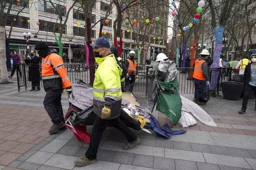 Workers carry a tent used by people experiencing homelessness to a garbage truck, Friday, March 11, 2022, during the clearing and removal of several tents at an encampment in Westlake Park in downtown Seattle. Increasingly in liberal cities across the country — where people living in tents in public spaces have long been tolerated — leaders are removing encampments and pushing other strict measures to address homelessness that would have been unheard of a few years ago. (AP Photo/Ted S. Warr