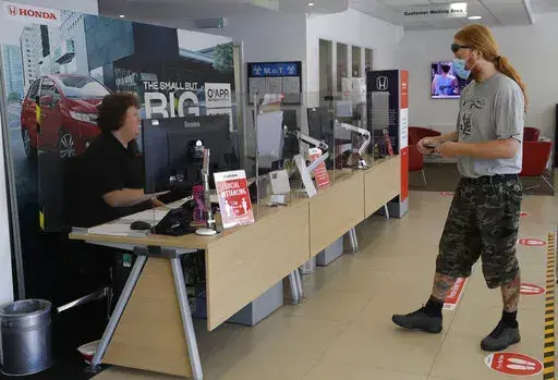 A customer wearing a face mask to protect against coronavirus, social distances in the car servicing department at the Trident Honda car dealership in Ottershaw, England, Friday, May 29, 2020. A new car warranty is a contract between the automaker and the vehicle owner. But if the owner doesn’t hold up his or her part of the bargain, it could void all the coverage. Here are a few reasons why your warranty claim can be denied and tips on how to avoid any issues down the road.  (AP Photo/Kirsty 