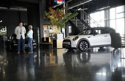 Prospective buyer chats with a sales associate as a 2022 Cooper S hardtop sits on the otherwise empty showroom floor of a Mini dealership Friday, May 6, 2022, in Highlands Ranch, Colo. As if buying a new car in today’s supply-constrained market wasn’t hard enough, this year, many shoppers are experiencing sticker shock when they realize that the car they wanted has a price tag well over the manufacturer’s suggested retail price. (AP Photo/David Zalubowski, File)